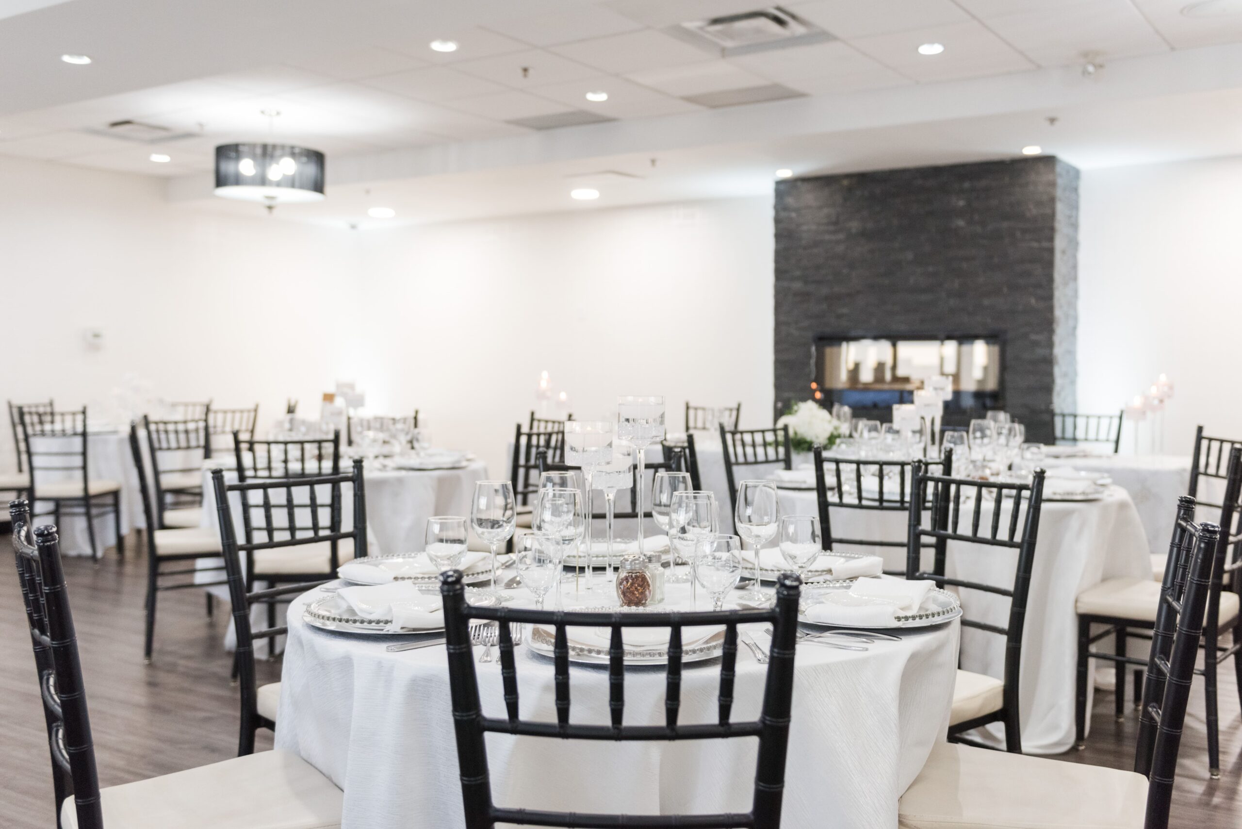 An elegantly set banquet hall with round tables, black chairs, and formal table settings, perfect for weddings.