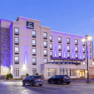 A modern hotel building illuminated at twilight, adorned for weddings, with parked cars in front.