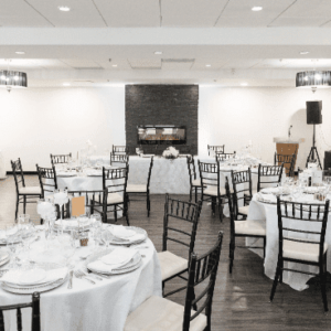 Elegant dining setup with black chairs and white tablecloths in a room with a fireplace.