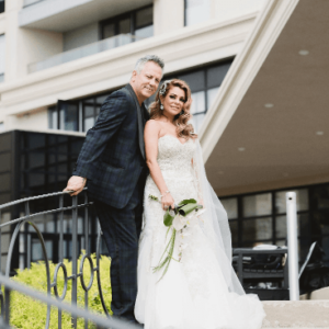 A couple in formal wedding attire posing for a photograph outdoors, with the bride holding a bouquet at their wedding.