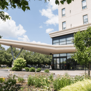 Modern building with an elevated walkway connecting two structures, ideal for weddings, surrounded by greenery under a partly cloudy sky.