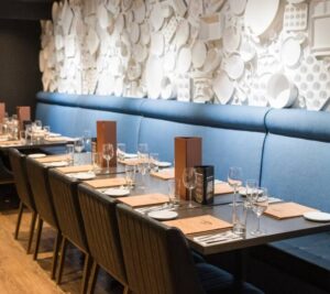 An elegantly set restaurant table, prepared for weddings, with a unique wall decorated with white plates and kitchenware.