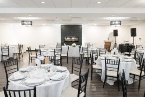 An elegantly set banquet hall with round tables, white linens, and a fireplace, ideal for weddings.