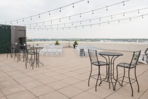 Rooftop terrace with string lights, metal tables and chairs, perfect for weddings, and a view of the skyline.